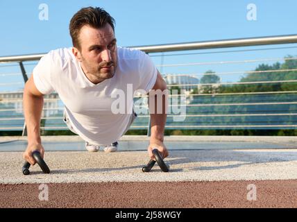 Close-up of a determined handsome middle aged Caucasian man, athlete exercising outdoor, pumping muscles while performing push-ups training on the urb Stock Photo