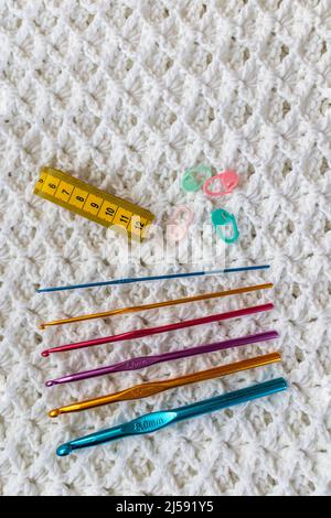 White embossed crochet stitch pattern as a background, a set of metallic blue, gold, purple and red crochet hooks of different sizes, yellow measuring Stock Photo