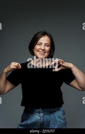 Positive middle aged woman wearing black t-shirt with empty space for your logo or text Stock Photo