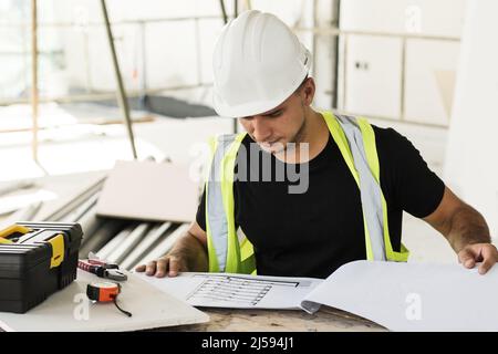 Young is worker checking blueprints during his work on a construction site Stock Photo