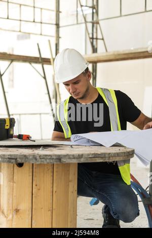Young is worker checking blueprints during his work on a construction site Stock Photo