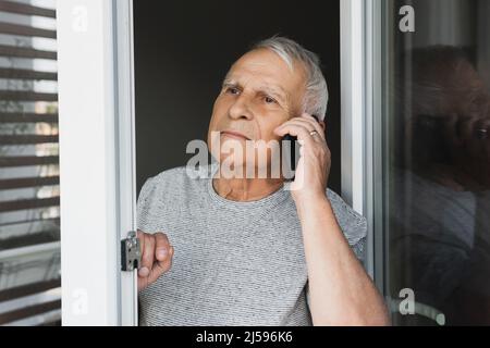 Suspicious elderly man looking into the window and make a call by smartphone Stock Photo