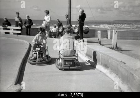 1960s, historical, at the seaside, two young children riding on battery powered mini go-karts at a concrete track, England, UK. Stock Photo