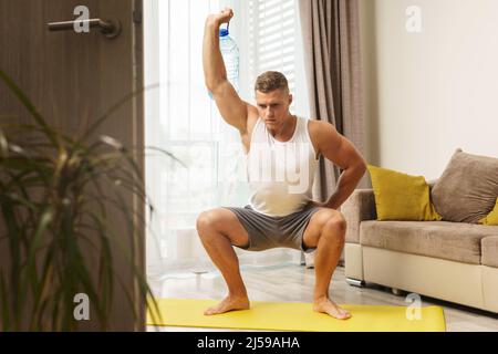 Young athletic man using big bottle of water like an alternative of dumbbell for home workout Stock Photo