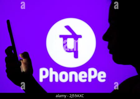 In this photo illustration the PhonePe logo seen in the background of a silhouetted woman holding a mobile phone. Stock Photo