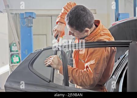 Auto service worker disassembles car door for repair, restoration. Stock Photo