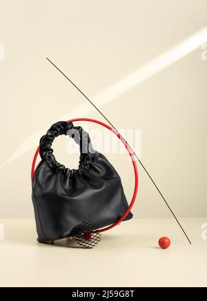Black handbag made from an artificial leather on a beige background with sun's rays. Idea of suprematism. Conceptual creative modern Still life Stock Photo