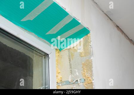 Fragment of a window with a plastic slope made of insulated panels covered with a protective film. Repair of a house or apartment. Finishing with sand Stock Photo