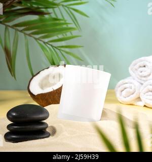Composition of coconut wax candles and SPA accessories on the beach sand. A trendy concept of a tropical scented candle, coconut and beach towel. Stock Photo