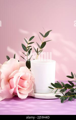 Composition of flowers and handmade candle made of eco- and vegan soy wax on a pink background. Soy candle with rose and leaves on a light purple Stock Photo