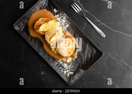 Cottage cheese pancakes, Syrniki or Cheesecakes with dried pineapple and caramel isolated on black marble background. Homemade food. Tasty breakfast. Stock Photo