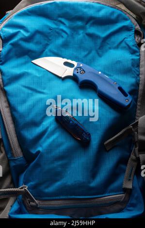 Blue knife and blue backpack. Blue knife on a blue background. Knife with a small blade. EDC knife. Stock Photo