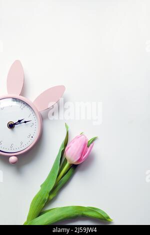 pink vintage alarm clock with beautiful tulip flower. Top view selective focus on white background Stock Photo