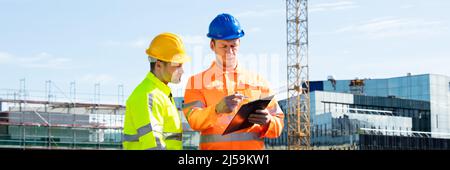 Male Architect Giving Instructions To His Foreman On Clipboard Working At Construction Site Stock Photo