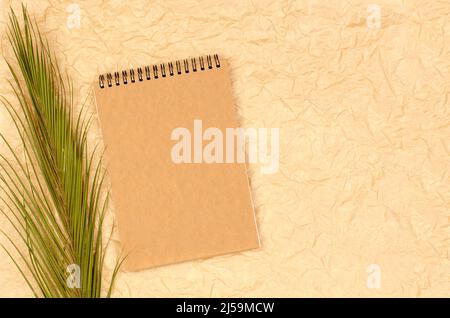 Blank notepad with kraft paper on crumpled beige background with palm leaves. Form for congratulations or invitations. Stock Photo