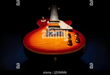 Beautiful product photo of a red orange brown cherry sunburst solid body electric guitar on a dark (black) background. Stock Photo