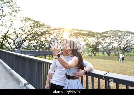 Couple taking a selfie from a park during sunset Stock Photo