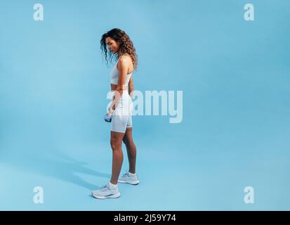 Fit woman posing on blue background. Side view of young sports woman relaxing. Stock Photo