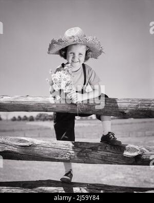 1940s SMILING LITTLE GIRL WEARING STRAW HAT LOOKING AT CAMERA CLIMBING OVER A WOODEN FARM FENCE HOLDING A BOUQUET OF DAISIES - j1966 HAR001 HARS BALANCE SAFETY PLEASED JOY LIFESTYLE FEMALES RURAL HEALTHINESS COPY SPACE FULL-LENGTH PHYSICAL FITNESS INSPIRATION FARMING RISK CONFIDENCE B&W EYE CONTACT DAISIES ACTIVITY HAPPINESS PHYSICAL WELLNESS CHEERFUL ADVENTURE STRENGTH FARMERS RECREATION PRIDE SMILES CONCEPTUAL FLEXIBILITY JOYFUL MUSCLES STYLISH GROWTH JUVENILES BLACK AND WHITE CAUCASIAN ETHNICITY HAR001 OLD FASHIONED Stock Photo