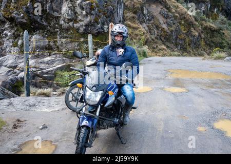 A man on his motorcycle, with his dog poke its head out of his coat.  Colombia, South America. Stock Photo