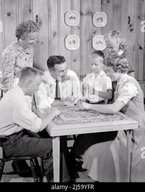 1950s FAMILY OF 6 WORKING ON JIGSAW PUZZLE IN A KNOTTY PINE PANELED RECREATION ROOM DAD MAKING A FUNNY FACE LAUGHING - j3385 HAR001 HARS FUN MAKING LADY LAUGHING HUSBAND 3 DAD FOUR MOM CLOTHING NOSTALGIC PAIR 4 MOTHERS GRANDMOTHER OLD TIME NOSTALGIA BROTHER OLD FASHION SISTER 1 JUVENILE STYLE TEAMWORK COMPETITION PUZZLE SONS GRANDPARENTS PINE PLEASED FAMILIES JOY LIFESTYLE SATISFACTION FIVE JIGSAW FEMALES MARRIED GRANDPARENT BROTHERS SPOUSE HUSBANDS HOME LIFE 6 COPY SPACE FRIENDSHIP HALF-LENGTH LADIES DAUGHTERS PERSONS MALES TEENAGE GIRL SIX TEENAGE BOY SIBLINGS SISTERS FATHERS PIECES B&W Stock Photo