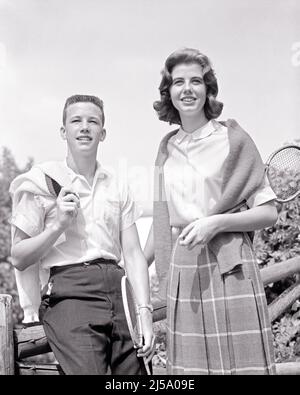 1960s SMILING TEEN BOY & GIRL HOLDING TENNIS RACQUETS SWEATERS DRAPED CASUALLY OVER SHOULDERS LOOKING AT CAMERA BOY HAS CREW CUT - j8647 HAR001 HARS PAIR ROMANCE SUBURBAN RELATIONSHIP CUT OLD TIME NOSTALGIA OLD FASHION FORWARD 1 JUVENILE CREW ATHLETE PLEASED JOY LIFESTYLE FEMALES HEALTHINESS COPY SPACE FRIENDSHIP HALF-LENGTH PERSONS MALES TEENAGE GIRL TEENAGE BOY ATHLETIC DRAPED B&W EYE CONTACT DATING SCHOOLS HAPPINESS CHEERFUL LEISURE UNIVERSITIES RECREATION CREW CUT ATTRACTION HIGH SCHOOL SMILES SWEATERS HIGH SCHOOLS HIGHER EDUCATION COURTSHIP JOYFUL STYLISH TEENAGED COLLEGES HAS POSSIBILITY Stock Photo