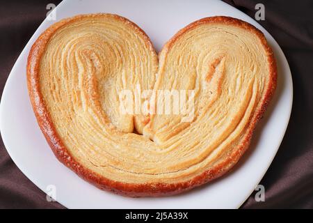 delicious ear-shaped puff pastry bread with sugar on a white ceramic homemade plate Stock Photo