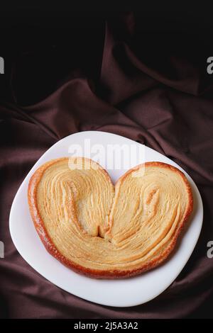 delicious ear-shaped puff pastry bread with sugar on a white ceramic homemade plate Stock Photo