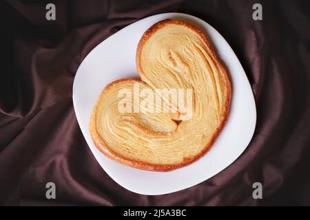 delicious ear-shaped puff pastry bread with sugar on a white ceramic homemade plate Stock Photo