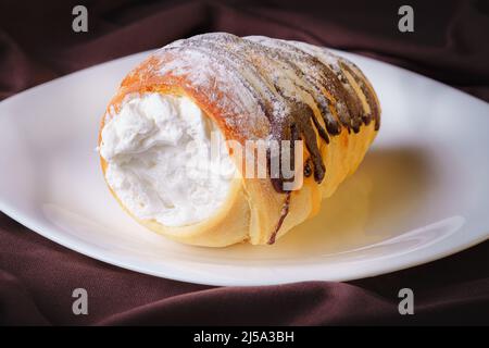 delicious rolled cone shaped bread filled with pastry cream covered with homemade chocolate and sugar placed on a white ceramic plate Stock Photo