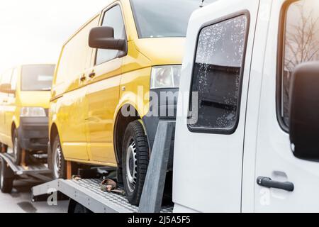 White small cargo truck car carrier loaded with two yellow van minibus on flatbed platform and semi trailer tow on roadside highway road. Volunteer Stock Photo