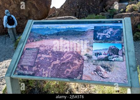 Petroglyph information sign, Rings Loop trail in Mojave National Preserve. A hiker looks at ancient rock art in Great Basin Curvilinear Abstract style Stock Photo