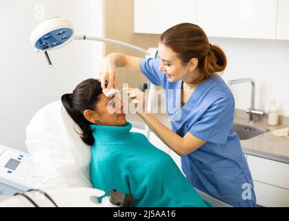 Beautician using white pencil and ruler for marking skin of latin woman Stock Photo
