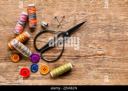 Sewing threads with buttons and scissors on wooden background Stock Photo