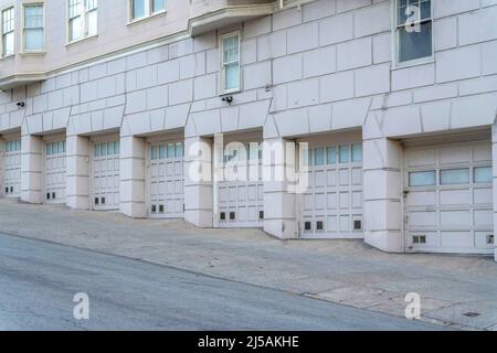 Residential building with sectional garage doors at San Francisco, California. Off-white building on a sloped land with old exterior designs. Stock Photo