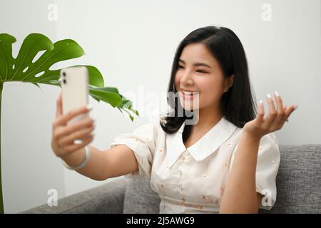 Charming Asian young woman taking herself photography via her smartphone in modern living room. Stock Photo