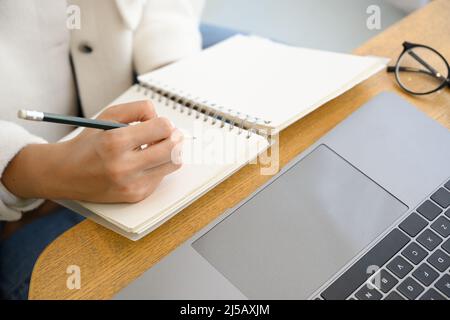 Cropped image, Female college student learning study on online via laptop computer and taking lecture on her empty spiral notebook. Stock Photo