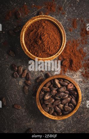 Cocoa beans and cocoa powder in wooden bowls on a black table. Top view. Stock Photo