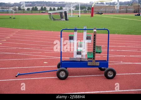 A rolling metal sports equipment rack with track and field running race starting blocks on an empty athletic track with lane markings. Shot outdoors i Stock Photo