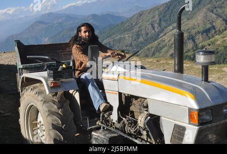 A south asian bearded and long haired man looking at camera while driving an old tractor in hilly area Stock Photo