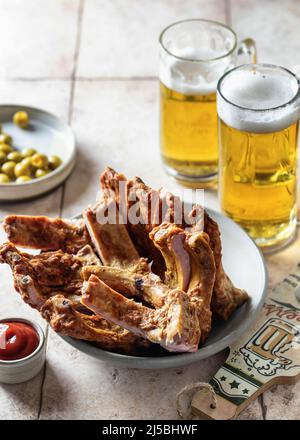 Smoked ribs on a platter, beer, bottle opener, sauce and olives. Party composition on pink tile background Stock Photo