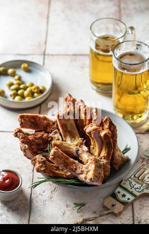 Smoked ribs on a platter with rosemary, two glasses of beer, bottle opener, sauce and olives. Party composition on pink tile background Stock Photo