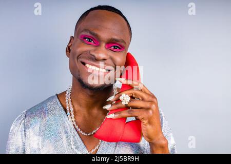 african american cross dressing trans drag queen holding a red shoe in studio white wall Stock Photo