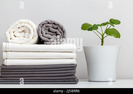 A stack of gray and white linens, sheets and towels on the table. Plant in the pot Stock Photo