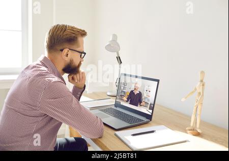 Serious man watching video lecture or having online class with remote teacher on laptop Stock Photo