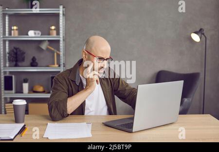 Focused businessman looking at laptop screen while reading important information on internet. Stock Photo