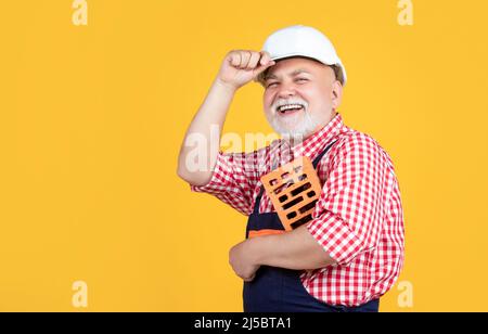 smiling senior man bricklayer in hard hat on yellow background Stock Photo