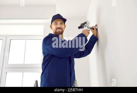 Male contractor installing surveillance cctv camera on wall in new bright office. Stock Photo