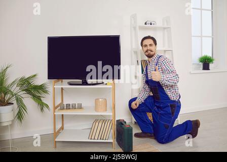 Happy technician showing thumbs up after he has fixed or installed modern TV set Stock Photo
