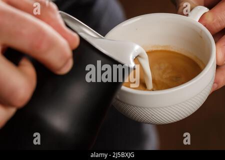 Professional barista pouring steamed milk into coffee glass cup making beautiful latte art Rosetta pattern in cafe. Flowing fresh ground coffee. Drink Stock Photo